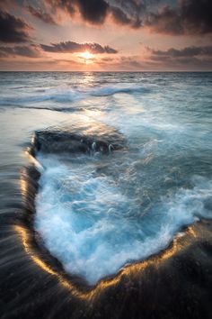 Phần này có thể chứa: the sun is setting over the ocean with waves crashing in front of it and dark clouds