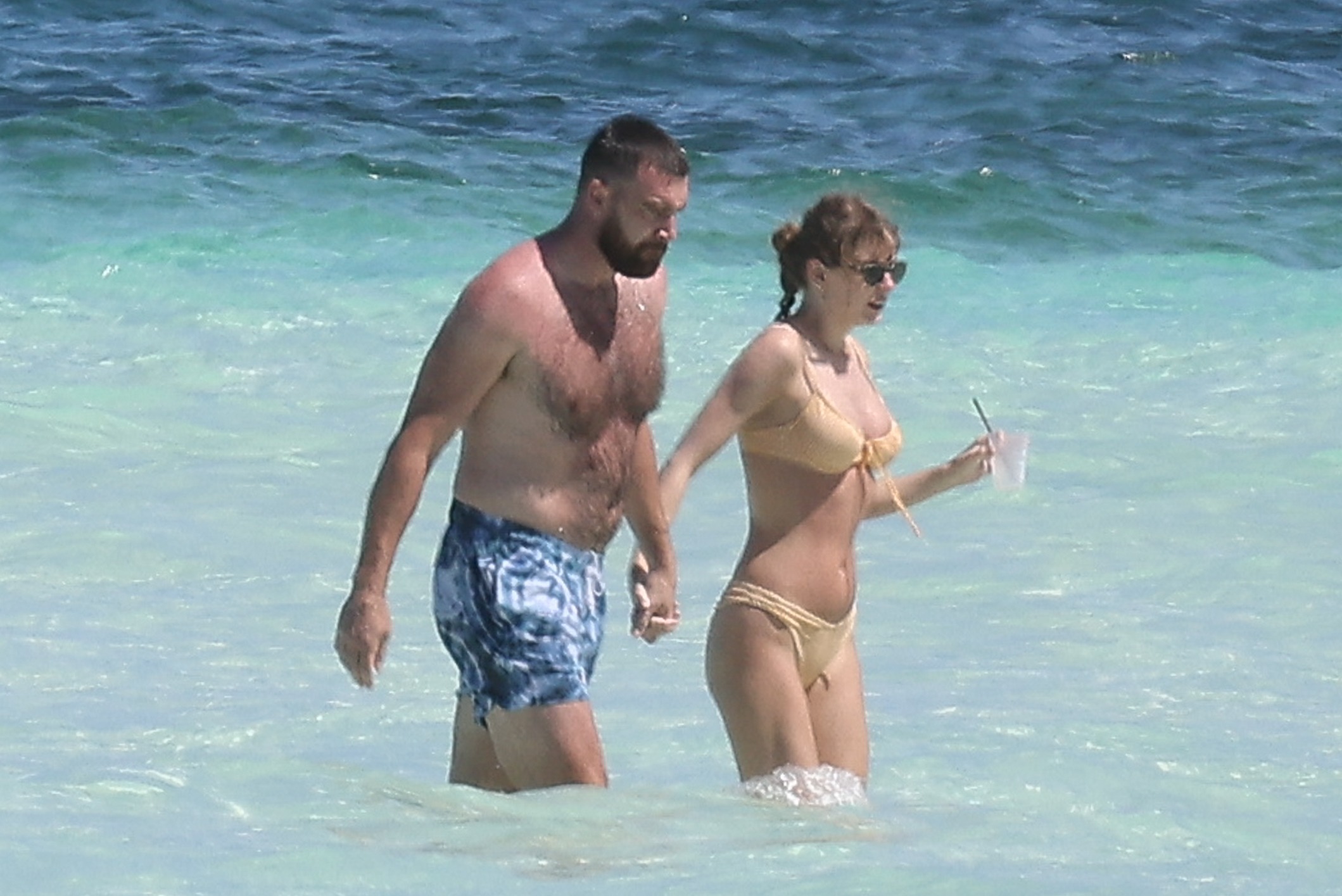 Travis Kelce and Taylor Swift holding hands in the ocean